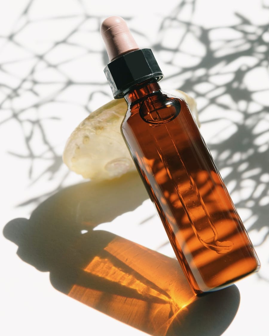 An amber dropper bottle lies in sunlight, casting a warm shadow.