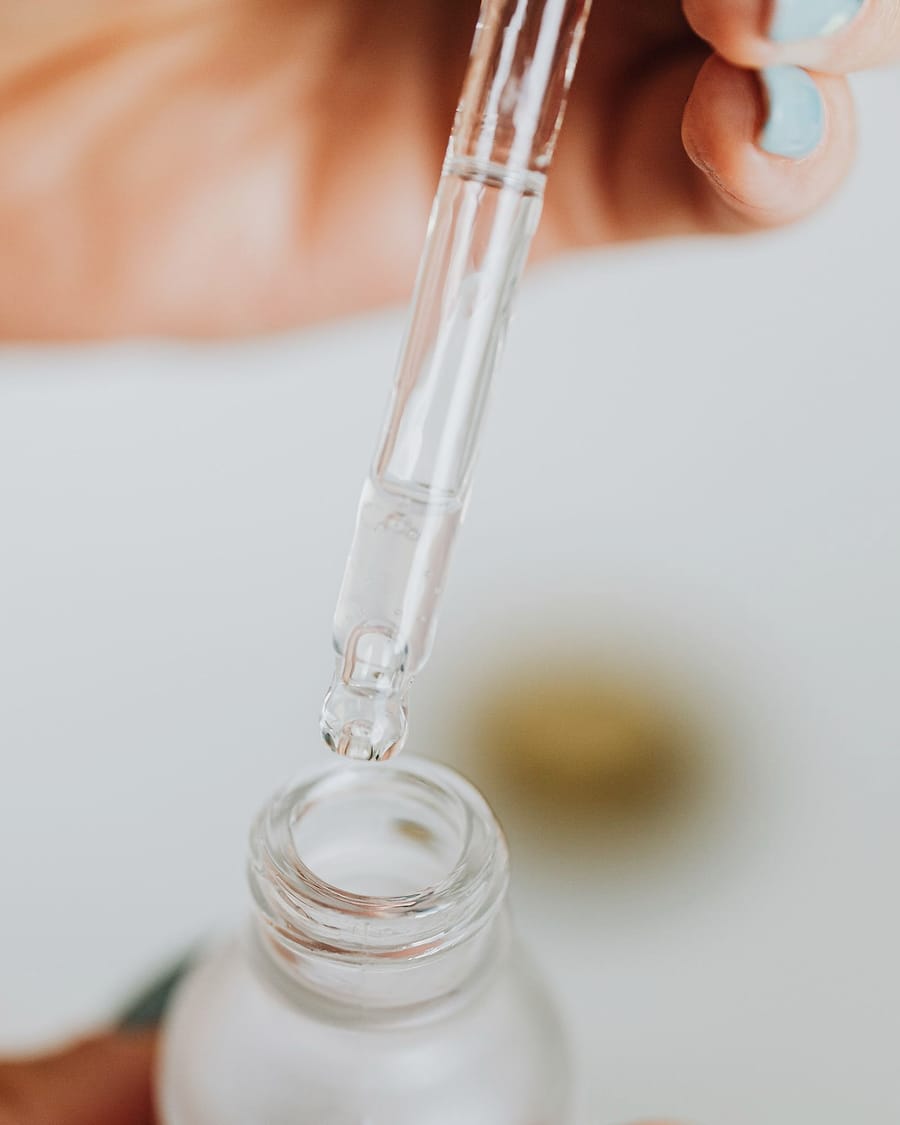 A glass pipette lifts a drop of serum from a small bottle.