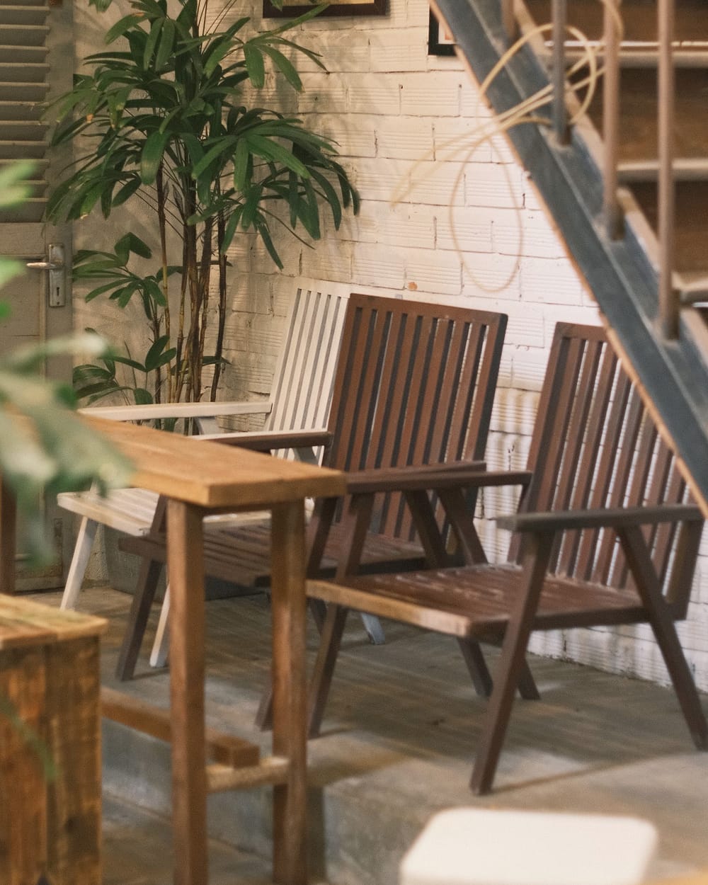 Wooden chairs around a small table, with plants by a white brick wall.